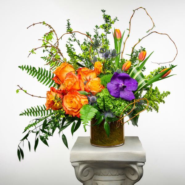 Orange roses and tulips with a purple orchid in a glass vase