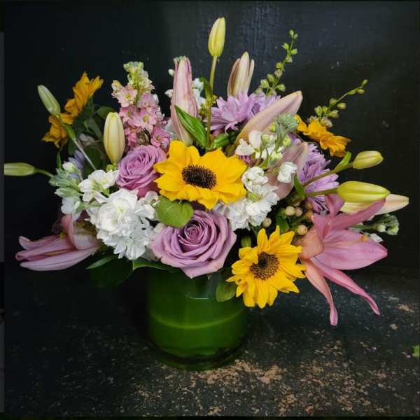 Mixed bouquet of sunflowers, lilies, roses, and lavender flowers in a green vase