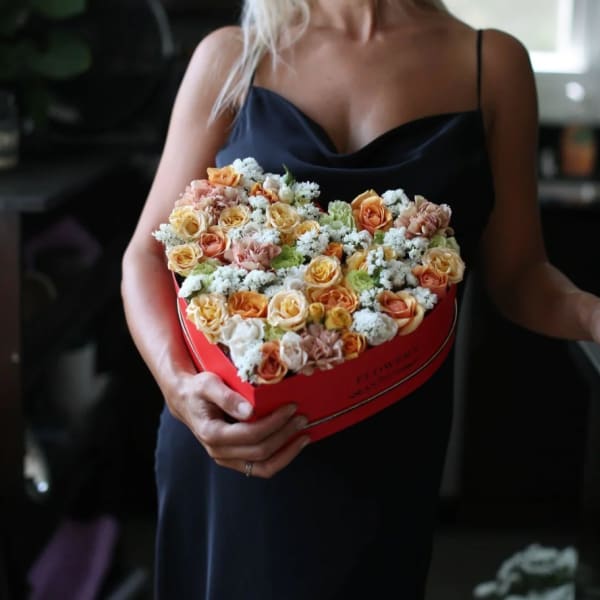 Woman holding a heart-shaped box of peach and white roses