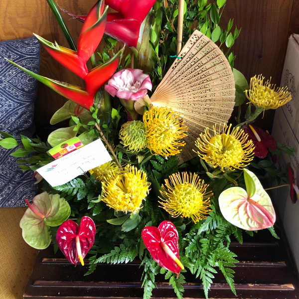 Tropical flower arrangement with red heliconia, yellow pincushion blooms, and an open fan
