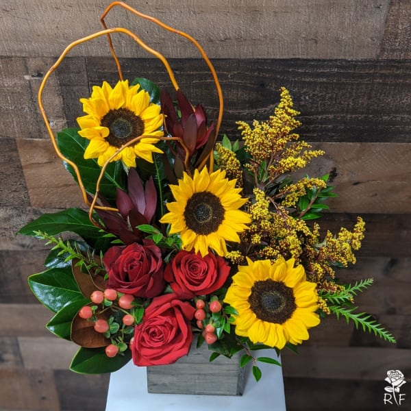 Sunflowers and red roses arranged in a gray box with orange curly branches