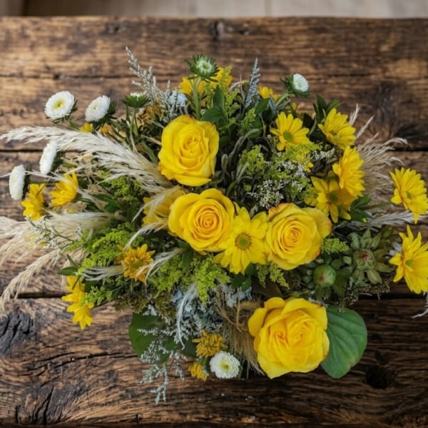 Low arrangement of yellow roses and daisies with white accents on a rustic wooden table