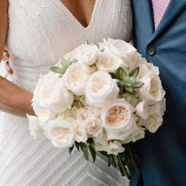Bride holding a white rose bouquet beside a man in a blue suit