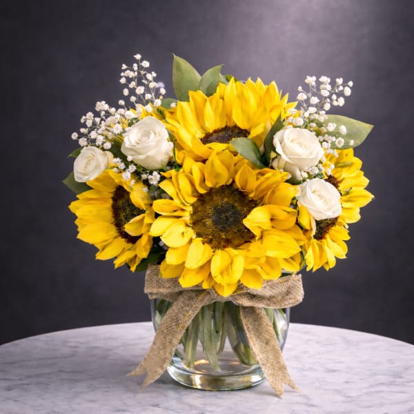 Sunflower and white rose bouquet in a glass vase with a burlap ribbon