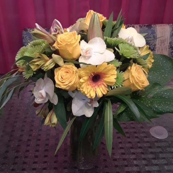 Bouquet of yellow roses, white orchids, and green chrysanthemums in a glass vase