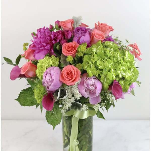 Bouquet of pink and coral flowers in a clear glass vase with a green ribbon