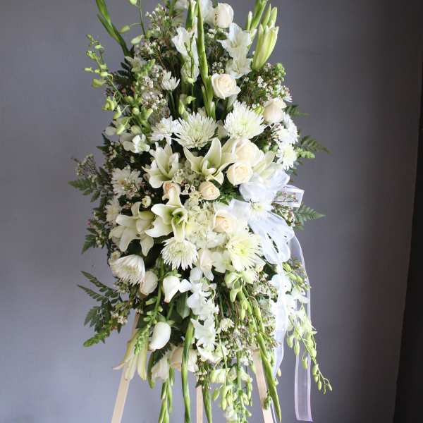 Tall white floral standing spray with lilies, roses, and ribbons
