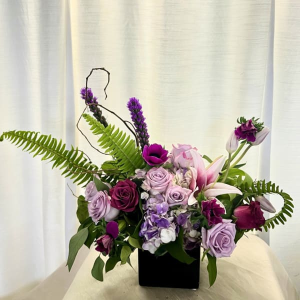 Purple and pink floral arrangement in a black square vase