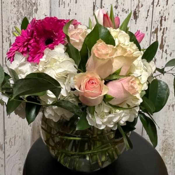 Bouquet of pink roses, white hydrangeas, and magenta gerbera daisies in a glass vase