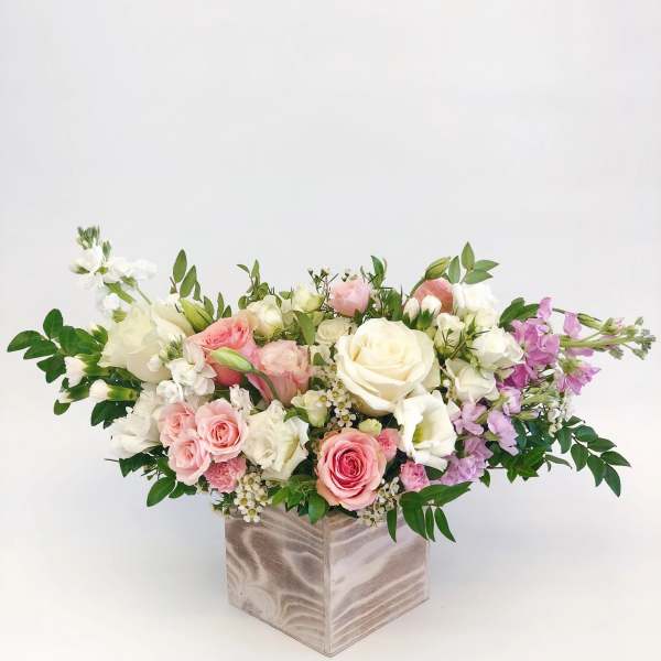Low floral arrangement of pink, white, and lavender roses in a square vase