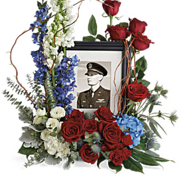 Floral tribute around a framed portrait with red roses and blue and white flowers