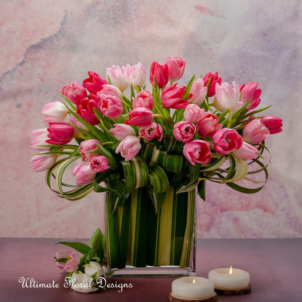 Pink and white tulips in a clear rectangular vase with candles nearby