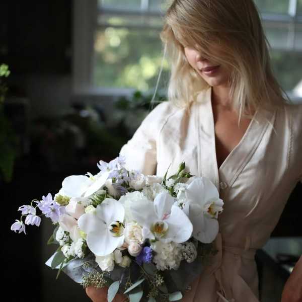 Woman holding a white and lavender bouquet with orchids and roses