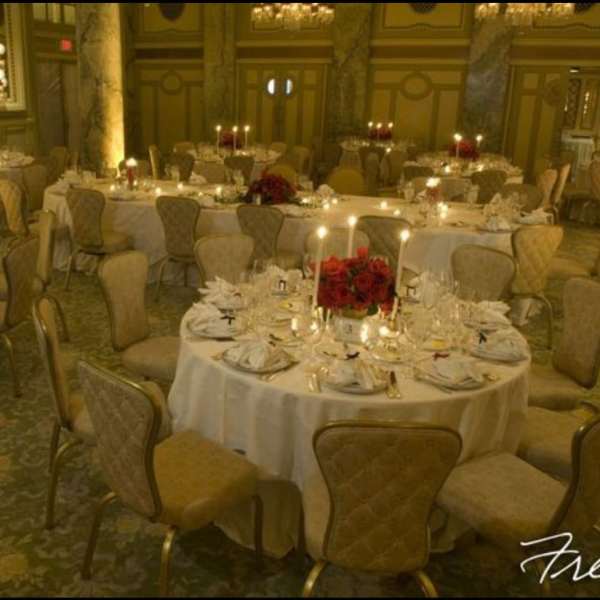 Round banquet tables with red floral centerpieces and candles in a formal hall