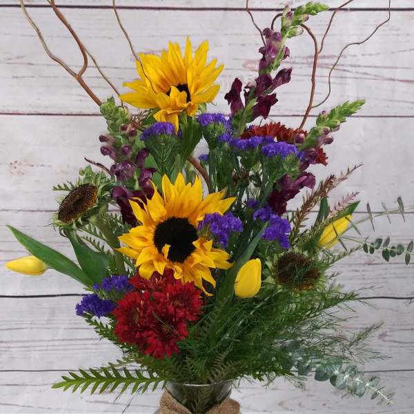 Mixed bouquet with sunflowers, tulips, and red blooms in a glass vase