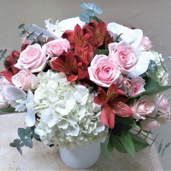 Bouquet of pink roses, white hydrangea, and red alstroemeria in a white vase