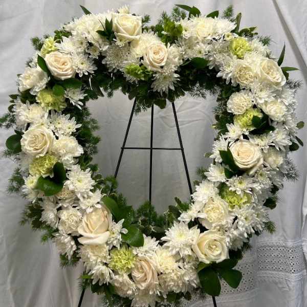 Heart-shaped white floral wreath on a black stand