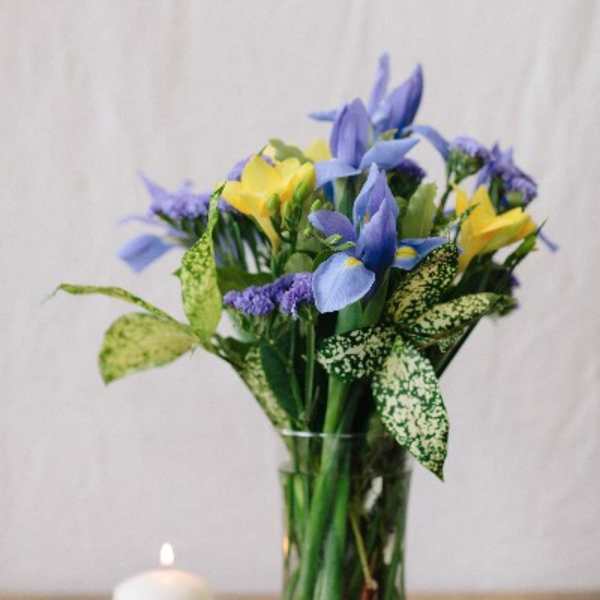 Blue and yellow flowers arranged in a clear glass vase beside a small candle