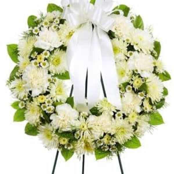 White floral wreath with a large white ribbon on a stand