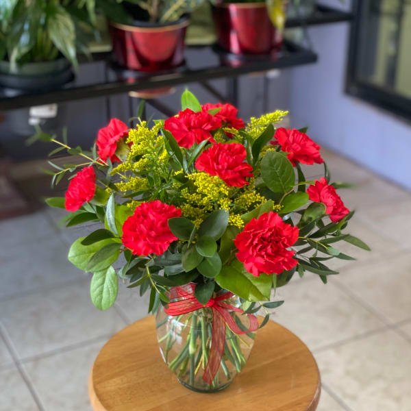 Red carnations in a glass vase with yellow filler flowers