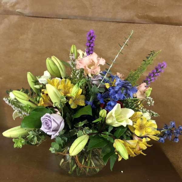Mixed bouquet in a glass vase with lilies, roses, and blue flowers