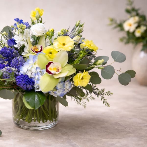 Mixed bouquet of yellow, blue, and white flowers in a glass vase