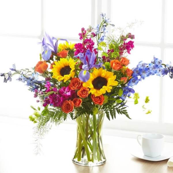 Mixed bouquet of sunflowers, roses, and blue flowers in a glass vase