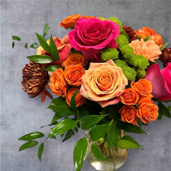 Bouquet of pink and orange roses with green button mums in a glass vase