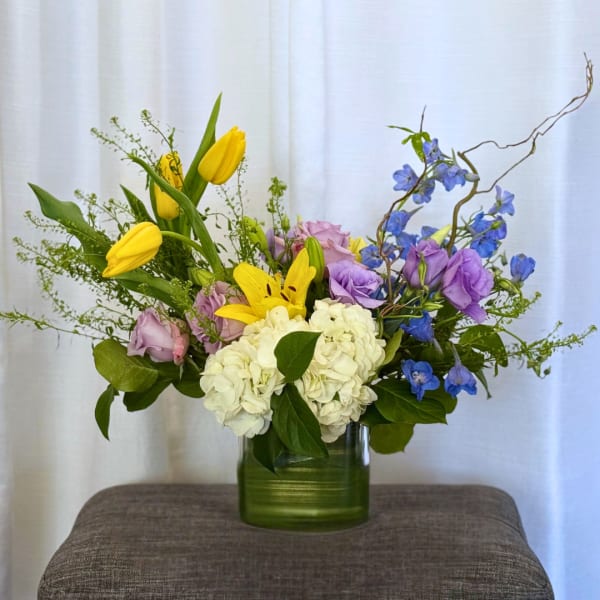 Mixed bouquet with yellow tulips, white hydrangea, and purple flowers in a green vase