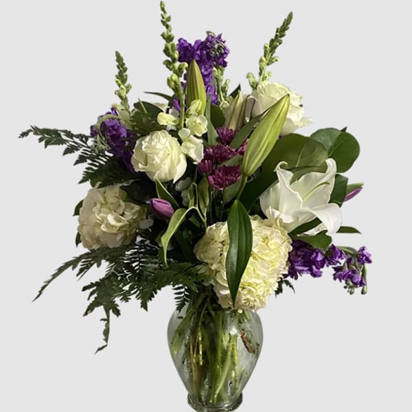 White and purple floral arrangement in a glass vase