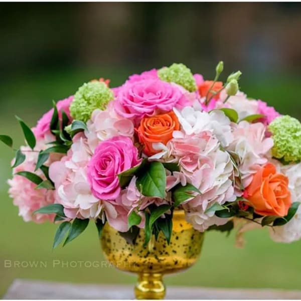 Pink and orange roses with pale hydrangeas in a gold vase