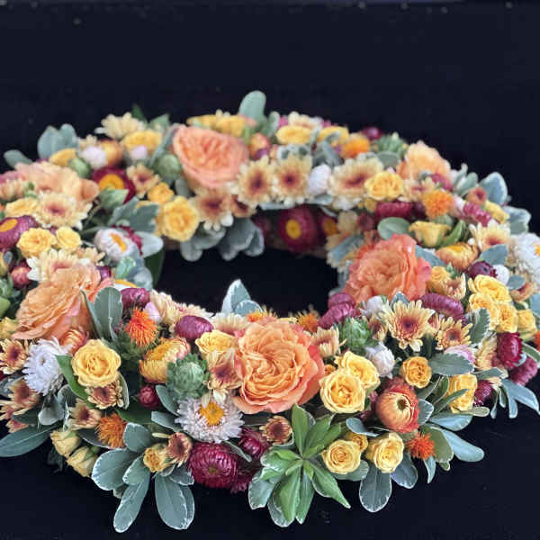Circular floral wreath with peach, yellow, and burgundy blooms on a dark background