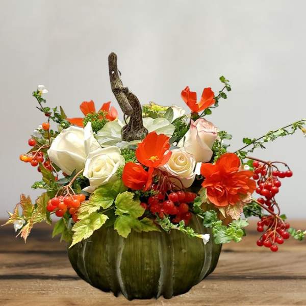 Orange and white floral arrangement in a green pumpkin vase