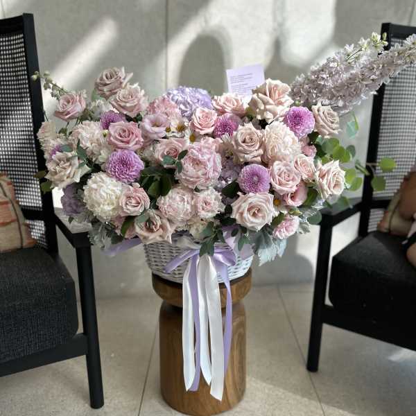 Large pastel flower arrangement in a white basket with ribbon