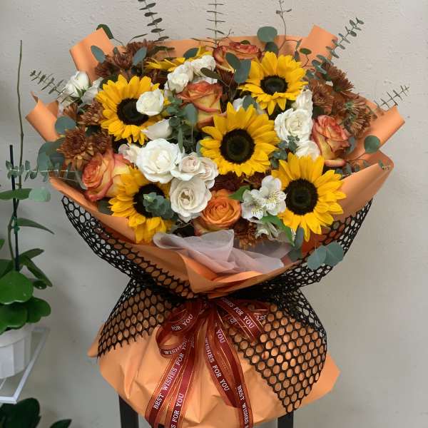 Bouquet of sunflowers, roses, and white blooms wrapped in orange paper