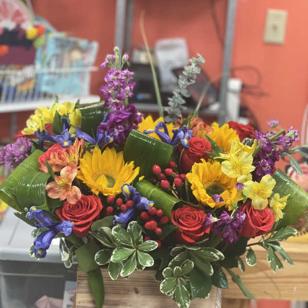 Colorful mixed bouquet with roses, sunflowers, and purple blooms in a wooden box
