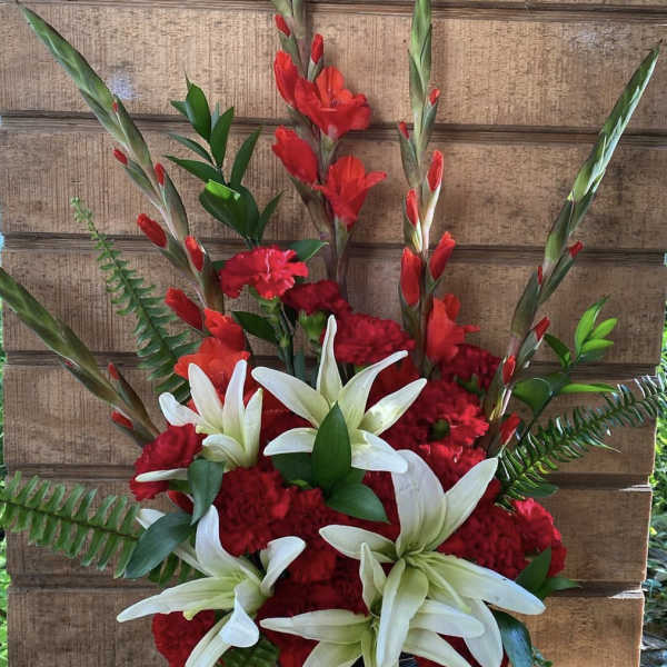 Tall red and white arrangement with lilies, carnations, and gladiolus in a black vase