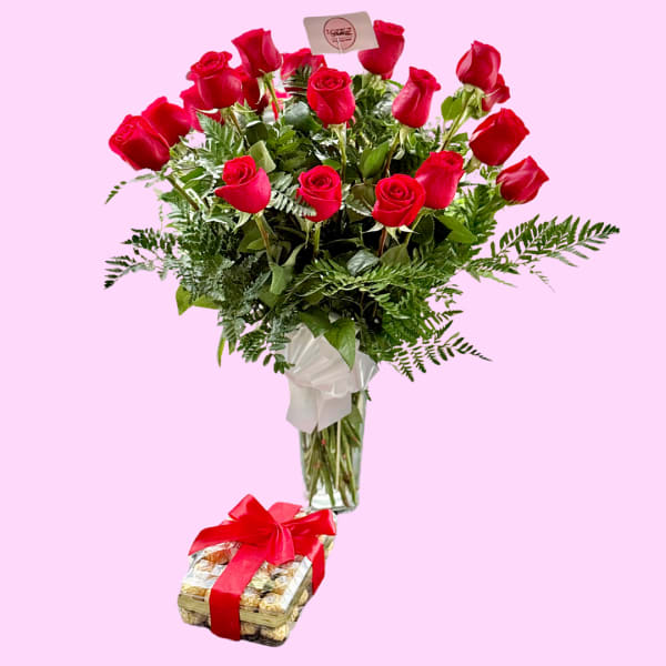 Red roses in a glass vase with a box of chocolates tied with a red ribbon