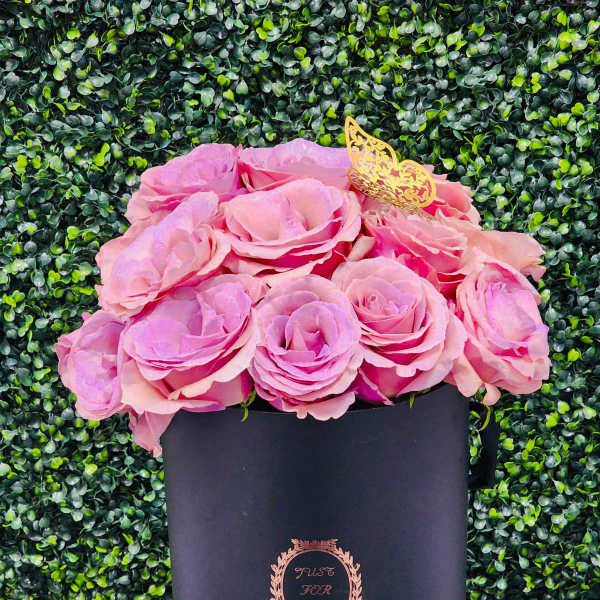 Pink roses arranged in a black hatbox with a gold butterfly topper