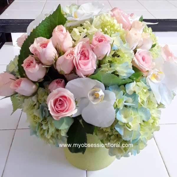 Pink roses and white orchids arranged with pale hydrangeas in a round vase