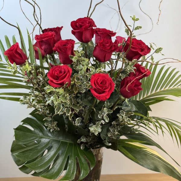 Tall arrangement of red roses with large tropical leaves in a clear glass vase