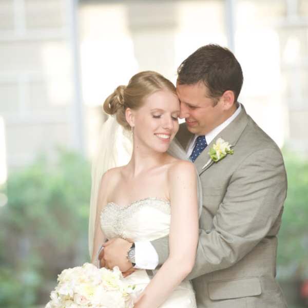 Bride holding a white and blush bouquet with groom behind her