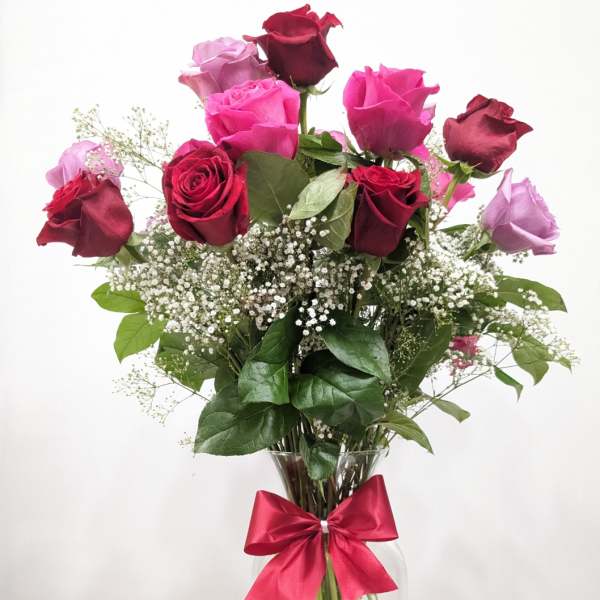 Bouquet of red, pink, and lavender roses in a glass vase with a ribbon