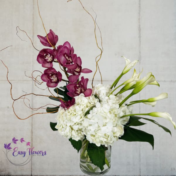 White hydrangeas and purple orchids in a clear glass vase with curly branches