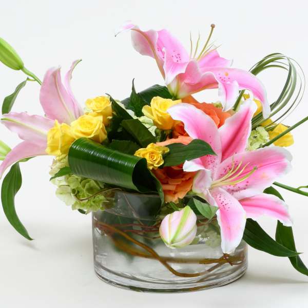 Pink lilies and yellow roses arranged in a clear glass vase