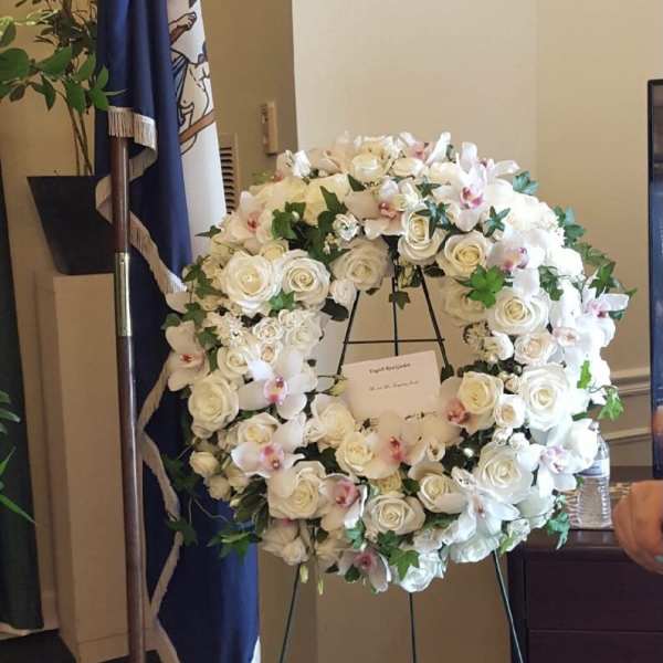 Large white floral wreath on an easel with roses and orchids