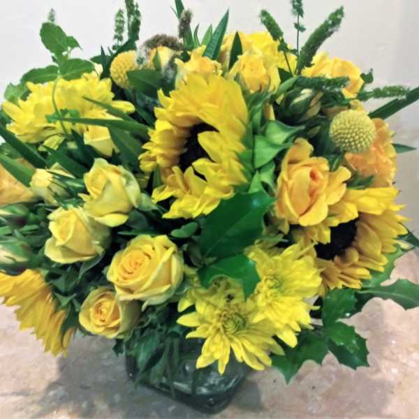 Yellow roses and sunflowers arranged in a glass vase