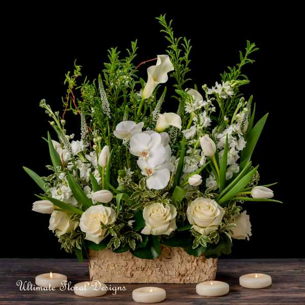 White floral arrangement with roses, orchids, and calla lilies in a bark container