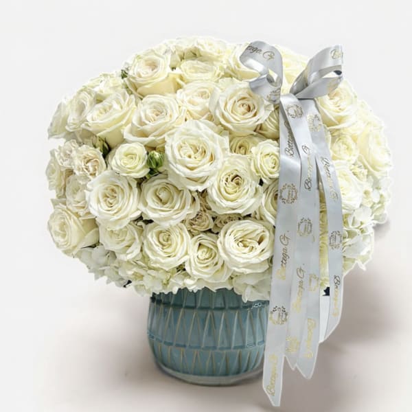 White rose bouquet in a blue glass vase with a silver ribbon