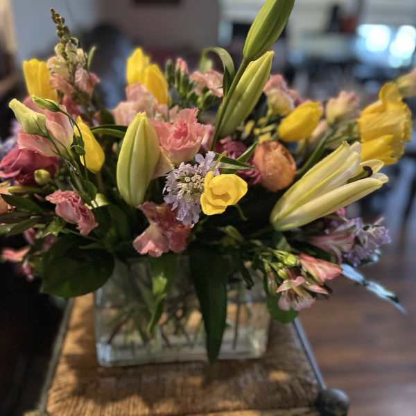 Mixed bouquet with yellow lilies, pink blooms, and a glass vase
